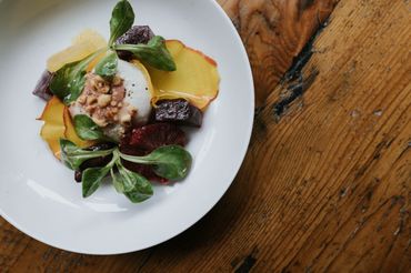 Gourmet salad with greens, nuts, and cheese on a white plate.