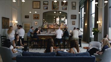 People socializing in a cozy, elegant bar with framed artwork and large windows.