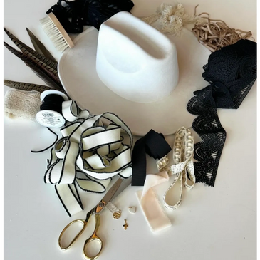 Hat-making supplies including ribbons, feathers, lace, scissors, and a white felt hat.