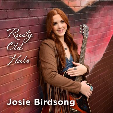 Josie Birdsong with guitar against a brick wall for Rusty Old Halo album.