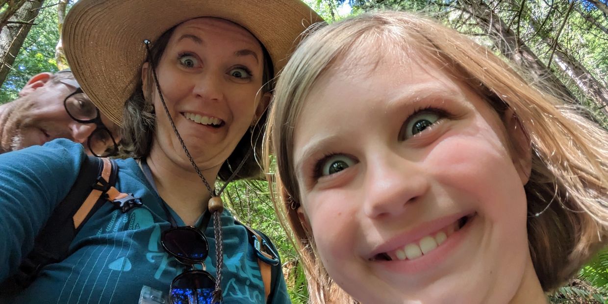 A playful family selfie with surprised and happy expressions in a forest.