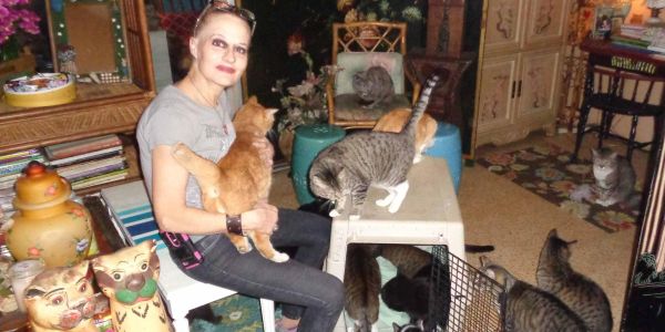 Woman sitting with multiple cats around her in a cozy room.