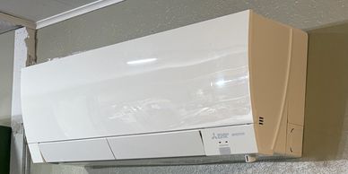 Wall-mounted white air conditioning unit above a beige wall with a curtain.
