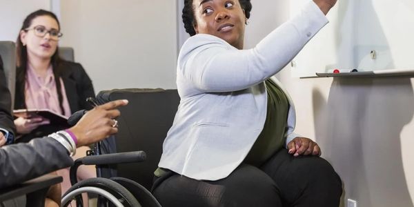 Woman in wheelchair leading a meeting at a whiteboard.