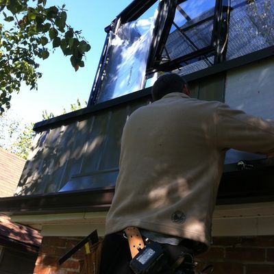 Man working on installing windows on a house under clear blue sky.