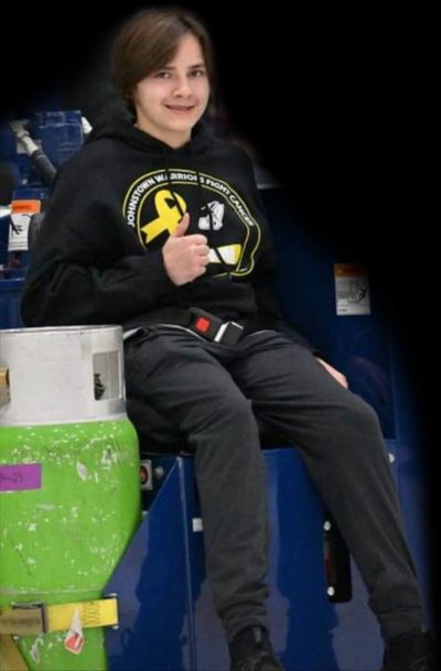Young person in casual black hoodie and pants sitting and smiling.