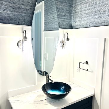 Modern bathroom corner with a blue vessel sink and oval mirror.