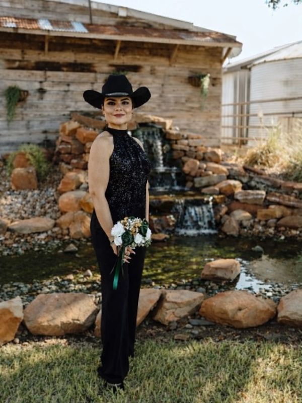 Woman in black dress and cowboy hat holding a small bouquet outdoors.