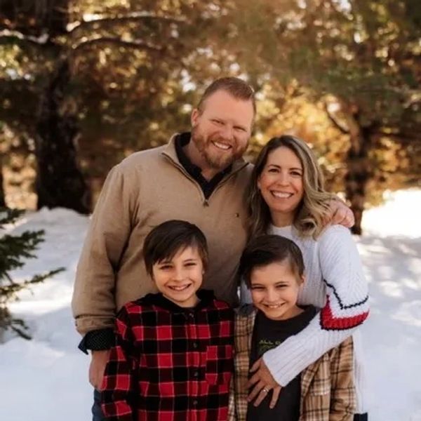 A smiling family of four posing outdoors in a snowy forest.