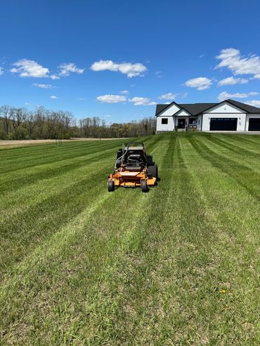 Riding lawn mower cutting grass in front of a house.