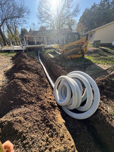 Construction site with trench and coiled pipe near a house.