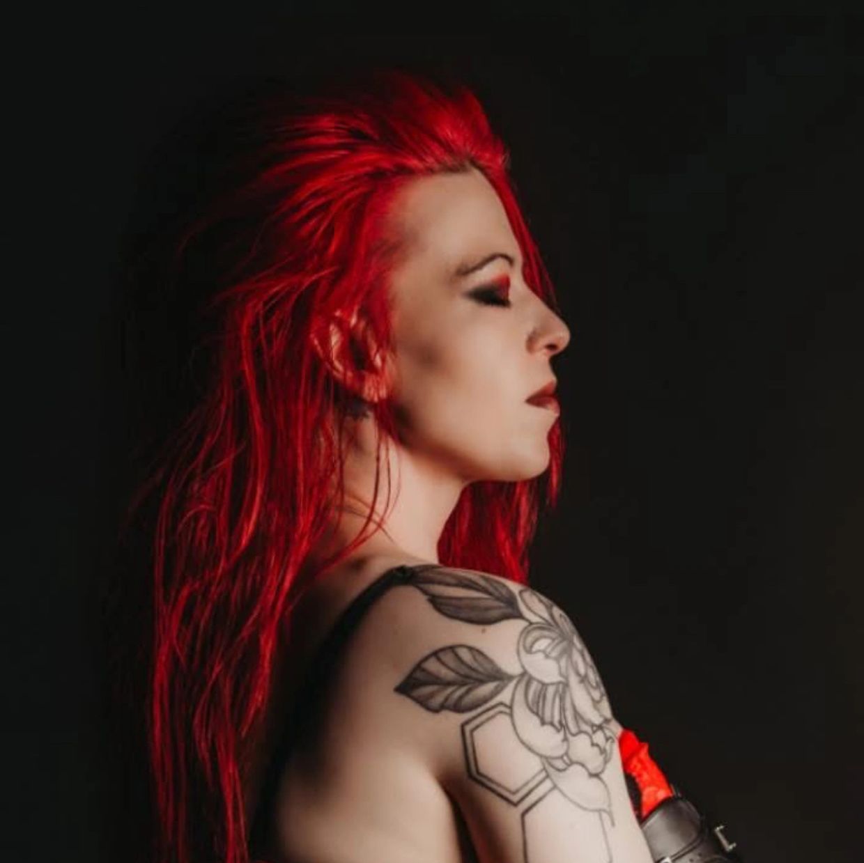 Woman with vibrant red hair and floral tattoo on shoulder.