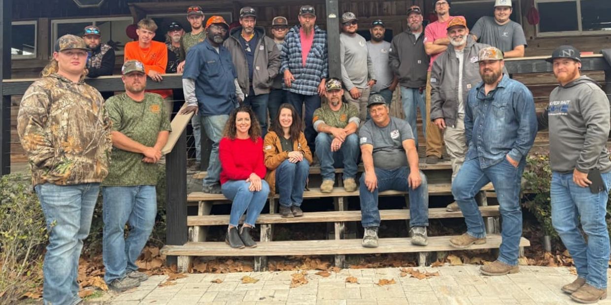 Large group of men and women posing on wooden steps outside.