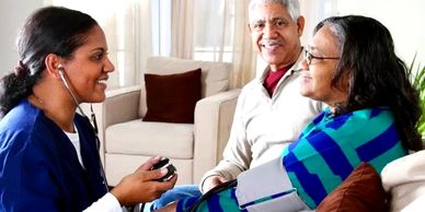 Nurse checking blood pressure of a smiling elderly woman with companion nearby.