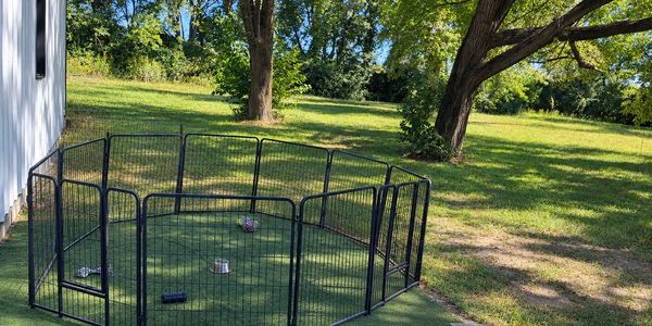 Outdoor pet playpen on grass with toys and water bowl.