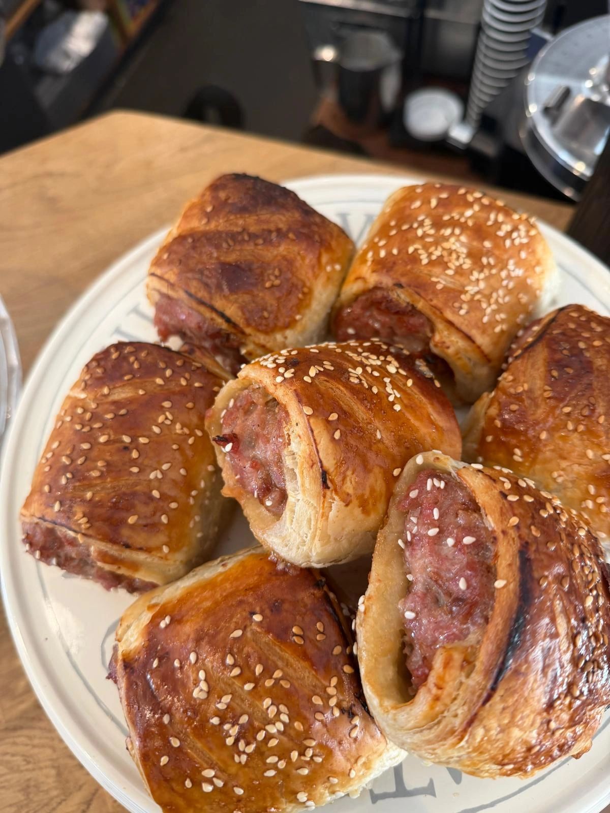 Plate of freshly baked sausage rolls topped with sesame seeds.