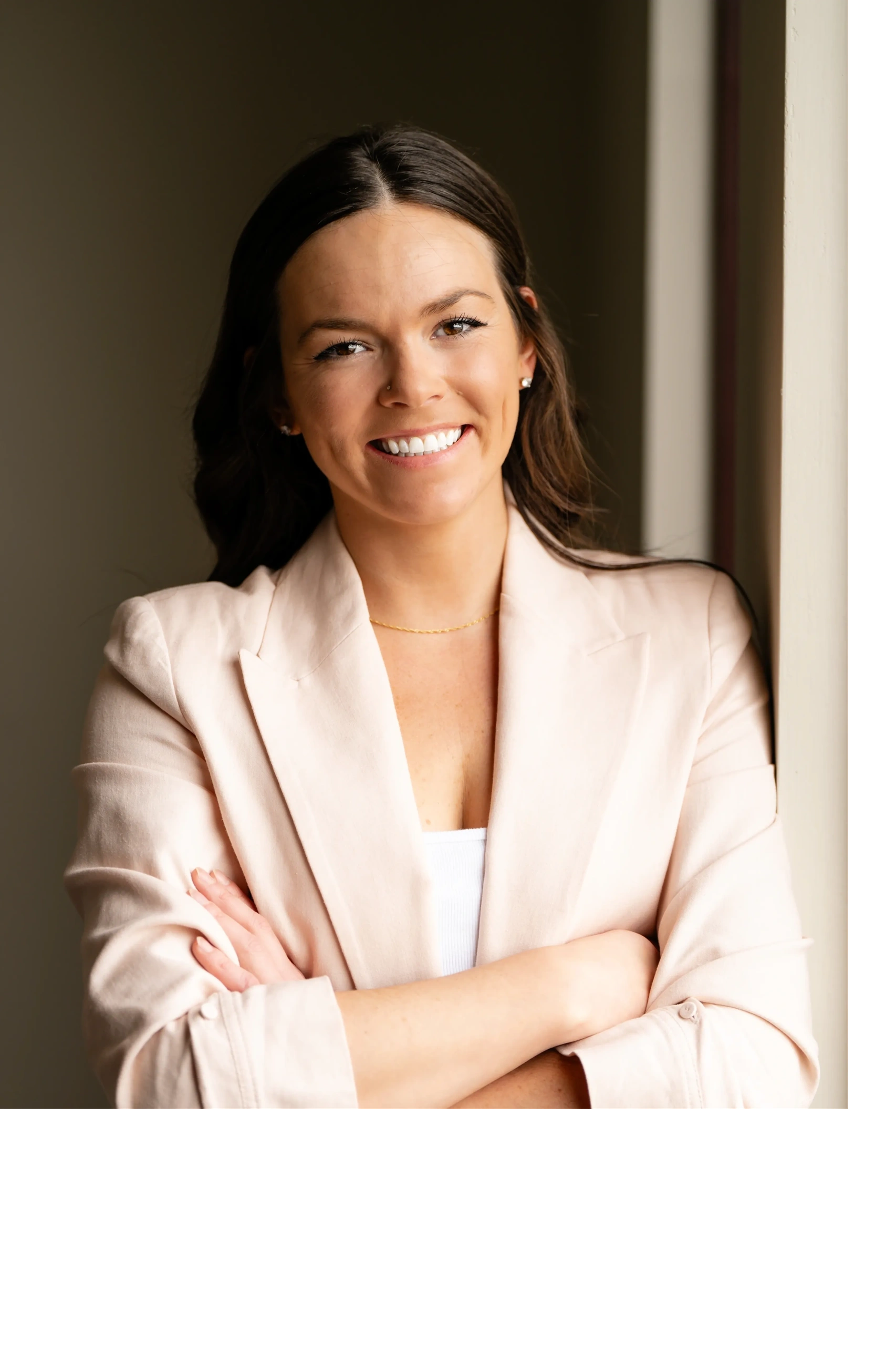 Smiling woman in a beige blazer with arms crossed.