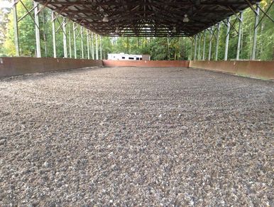 Covered outdoor arena with gravel surface.