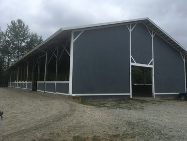 Large gray barn with white trim under a cloudy sky.