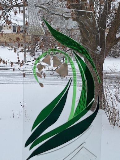 Stained glass artwork interpreting the flower called Lily of the Valley, suspended in a window. Whit