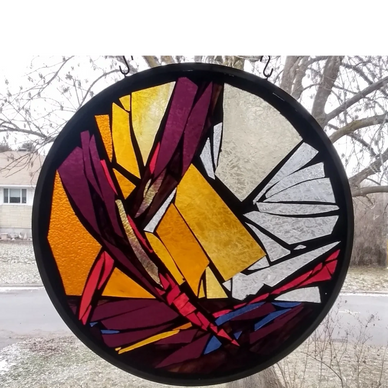 Framed circular stained glass art hanging in a window. Purple, red, blue, amber, yellow and clear gl