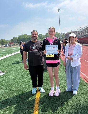 Runner holding a certificate with two supporters on a track field.