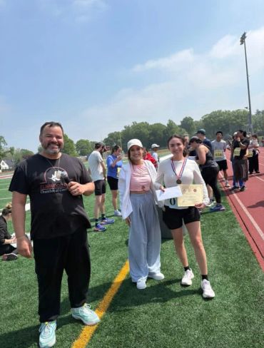 Three people posing on a track field, one holding an award certificate.