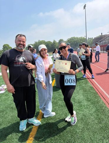 Three people smiling, one holding a certificate on a sports field.