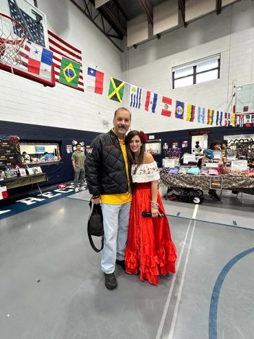 Man and woman posing in a gymnasium decorated with international flags.