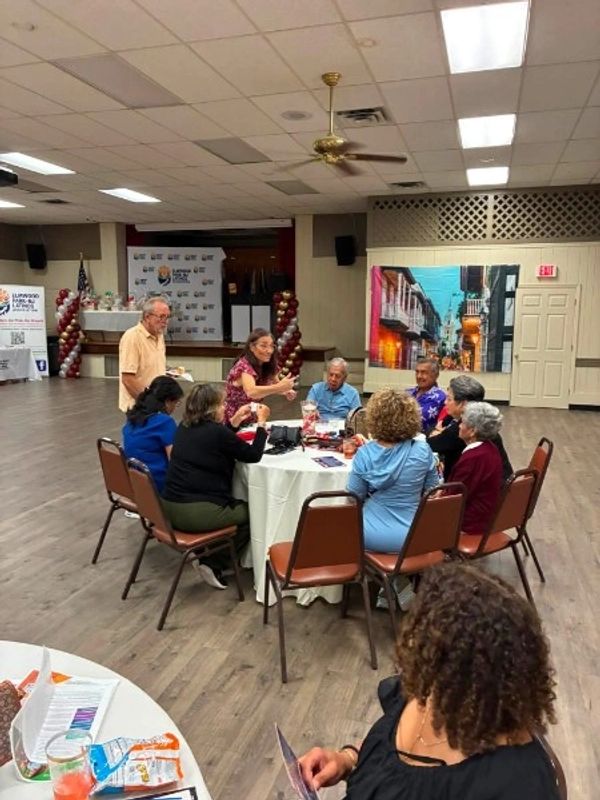 Group of people socializing around a table in a community hall.