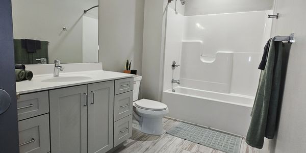 Modern bathroom with white bathtub, gray vanity, and wood-patterned floor tiles.