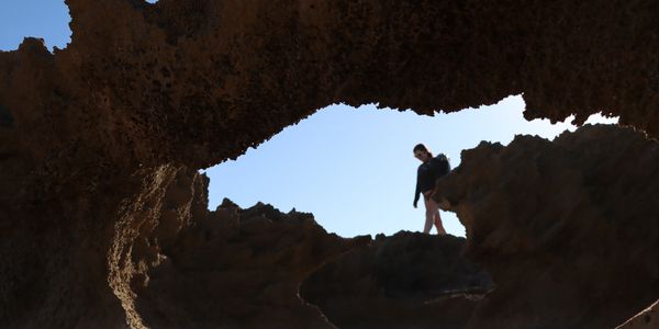 Person walking on rocky terrain seen through a natural rock arch.