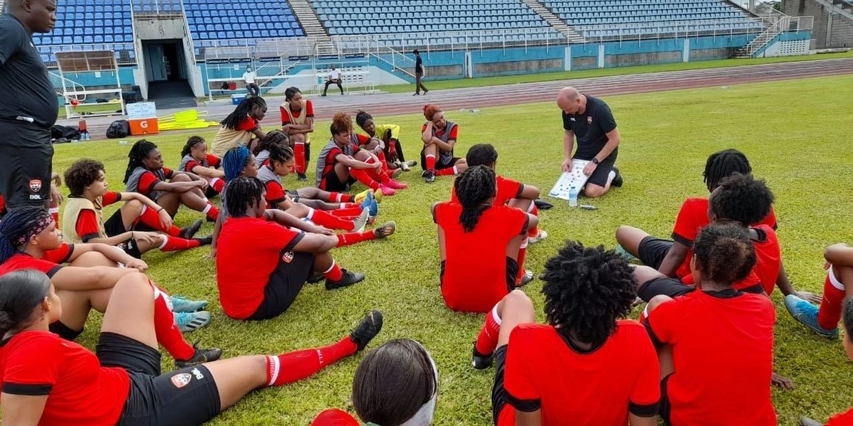 Soccer team sitting on field listening to coach's strategy.
