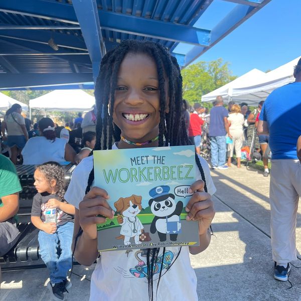 Young child holding the meet the workerbeez book at a Blue Hills community event