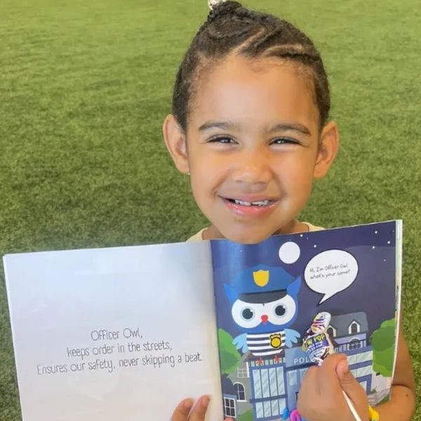 A little girl at a book fair holding the meet the workerbeez book to favorite character Officer Owl