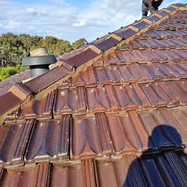 Worker repairing brown tiled roof under a partly cloudy sky.