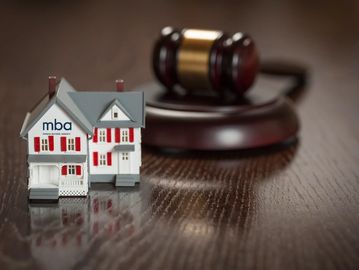 Miniature house with MBA logo and judge's gavel in background.