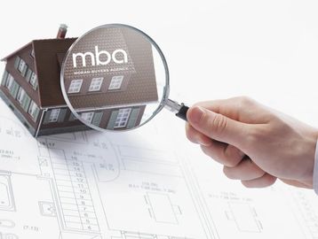 Hand holding a magnifying glass over a house model on architectural plans.