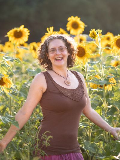 Dawn Gallahue standing in a field of sunflowers with arms open, smiling. 