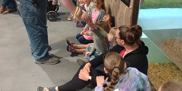 Children sitting on floor, engaging with an adult holding a snake.