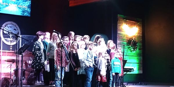 Children singing in a choir on stage during a performance.