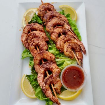 Grilled shrimp skewers served with lemon wedges and dipping sauce on a bed of lettuce.