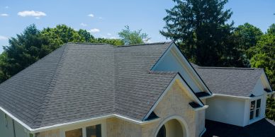 Modern house with a gray shingle roof surrounded by trees under a clear sky.