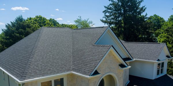 Modern house with a gray shingle roof surrounded by trees under a clear sky.