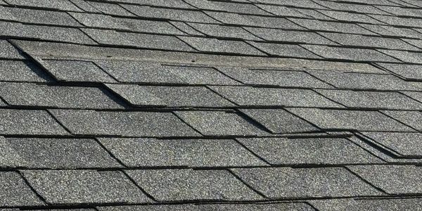 Close-up of a damaged asphalt shingle roof with visible lifting and curling.