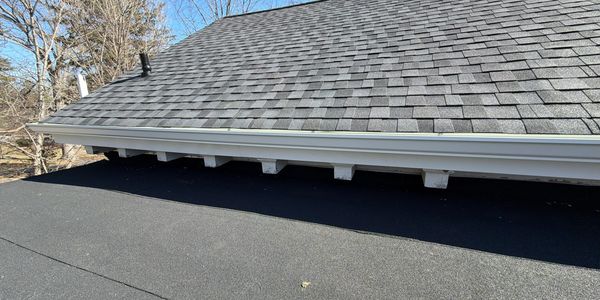Close-up of a roof edge with shingles and a black flat roof surface below.