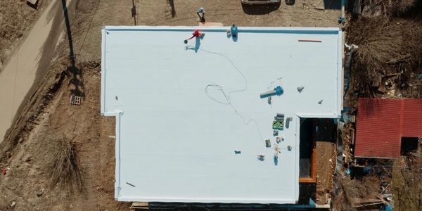 Aerial view of workers installing a white roof on a building.