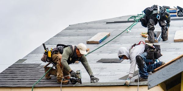 Three workers installing roofing shingles on a steep roof.
