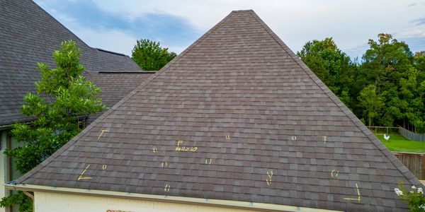 House roof with markings on shingles under a partly cloudy sky.