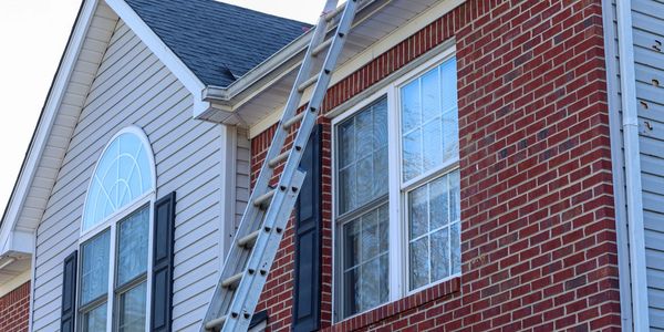 A ladder leans against a house with mixed brick and siding exterior.